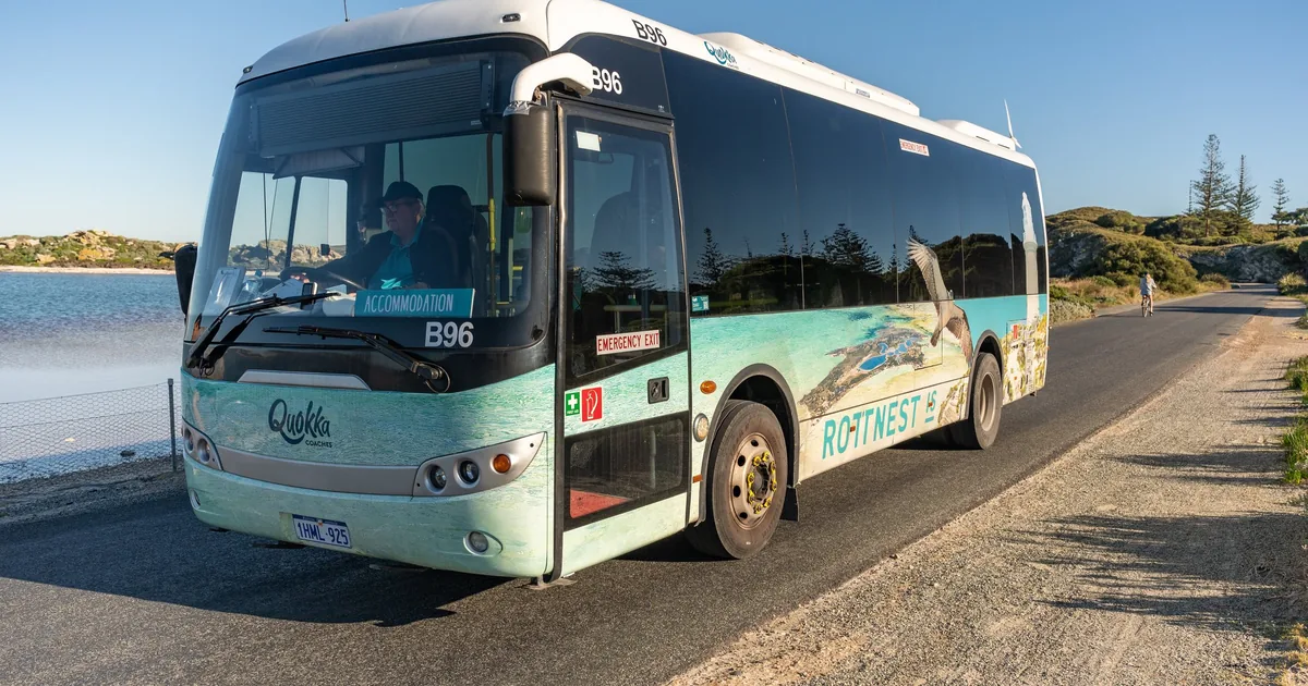 A white bus on a quiet road beside the water on Rottnest Island