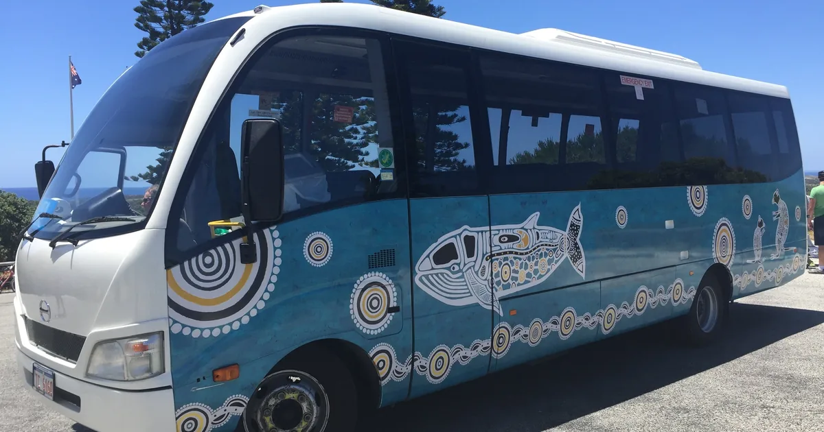 A blue and white tour bus with a painted design parked under tall pines on Rottnest Island